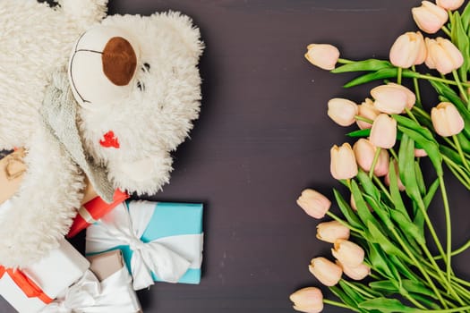 Tulip flowers with gifts and soft toy on dark as background