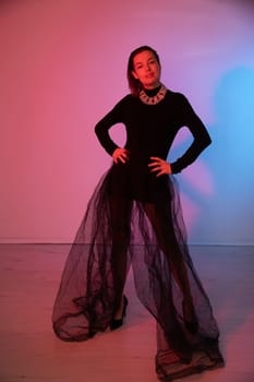 woman in black clothes in a tulle skirt poses on a pink background