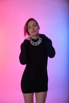 woman in a black dress poses on a pink background