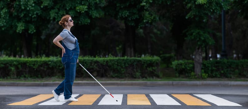 Blind pregnant woman crosses the road at a crosswalk with a cane