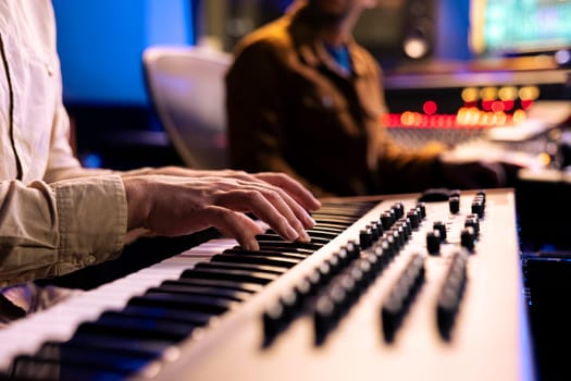 Male singer playing notes on electronic keyboard piano in music recording studio, producing a new hit with midi controller synthesizer. Skilled artist making a live performance in control room.