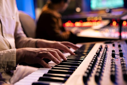 Artist performer recording his song on electronic keyboard piano, working with audio engineer in professional studio and producing new music. Singer composes on synthesizer. Close up.