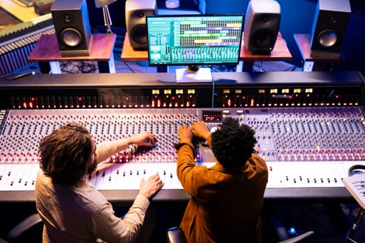 Musician and sound designer producing tunes on control panel board desk with daw software, professional recording studio. Team collaborating on hit songs, pressing buttons and sliders.