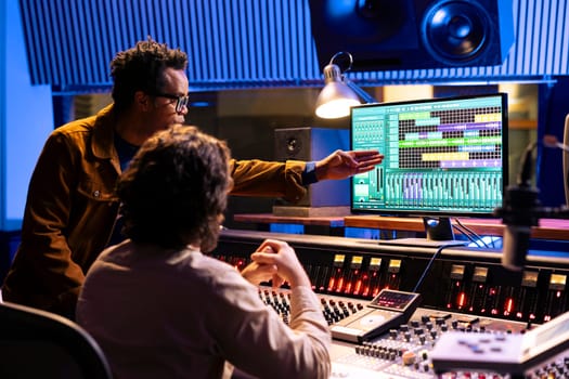 Diverse music experts mixing sounds on audio console and equalizer, adding sound effects and creating new tracks for an album. Artist and producer creating a hit song with daw software.