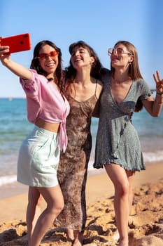 Group of smiling multiethnic women enjoying vacation. Beautiful and cheerful girls of generation z pose for a photo with a mobile phone.