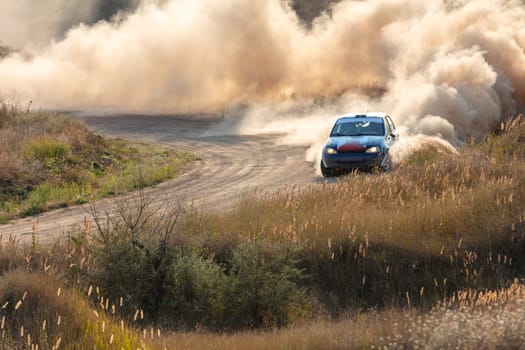 Sunny summer day. A sharp turn on a dirt rally track. A rally car creates clouds of dust
