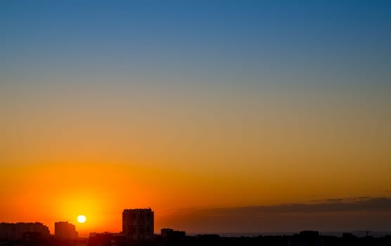 Clear skies over the silhouetted rooftops of a seaside town. The sun has just peeked over the horizon