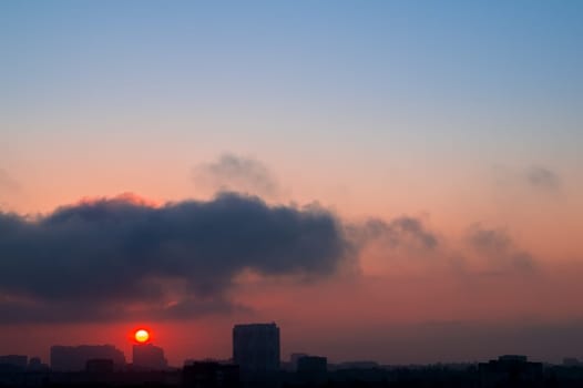 Dawn. Heavy cloud in the morning sky over the city. Silhouettes of buildings in the backlight