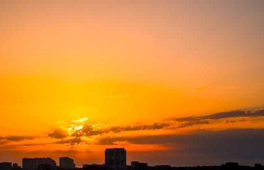 Sunrise over the city. The first rays of the sun through the clouds above the horizon. Silhouettes of buildings in backlight