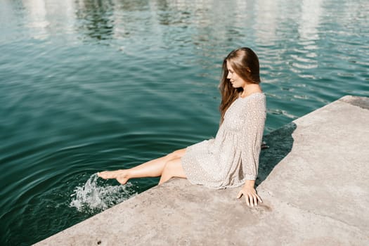 A woman is sitting in the water wearing a white dress. The water is calm and blue. The woman is enjoying the moment and taking in the beauty of the scene