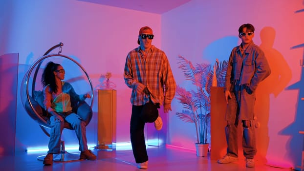 Happy hipster show break dancing while multicultural friend with casual cloth cheering at studio. Professional street dancer perform hip hop beat or lively rhyme with neon or led light. Regalement.