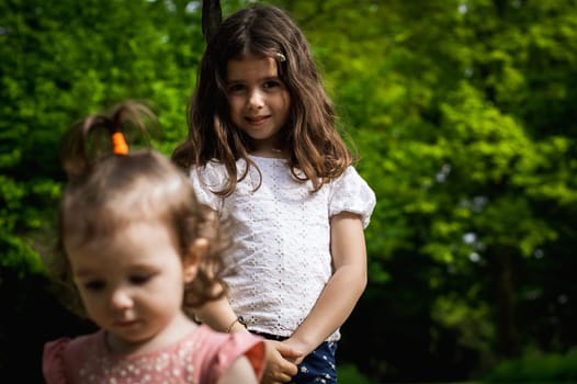 Portrait of one beautiful Caucasian happy smiling brunette woman with loose hair and black feather standing in the park on a spring day with her baby sister, side view close-up.