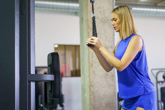 Side view horizontal photo of a beautiful woman exercising on a lat pulldown machine