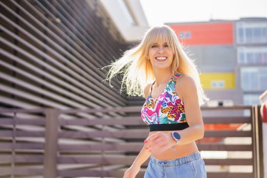 Horizontal three quarter length photo of a happy blonde woman dancing modern music in the city