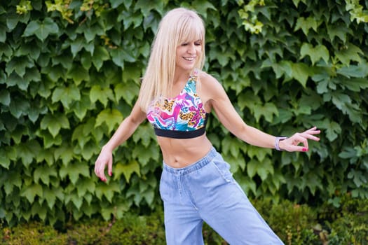 Blonde cute young woman expressing herself happily through dance next to an urban garden