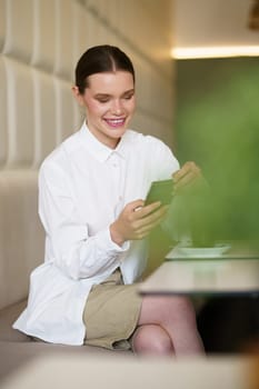 Vertical portrait of a beauty businesswoman smiling while using phone in a cafeteria
