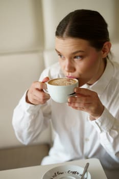 Vertical photo of an elegant caucasian adult woman drinking a cappuccino in a bar