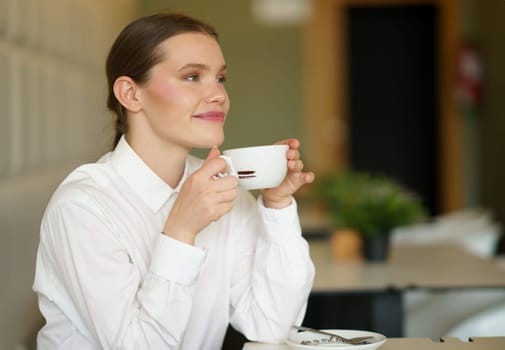 Side view of a beauty successful businesswoman enjoying coffee sitting alone in a cafeteria