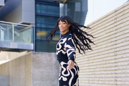 Hispanic beauty dancer with modern clothes turning moving her hair outside an urban building