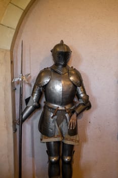 One set of knightly armor with a helmet and a sword stand near the wall in the medieval castle of the city of Luxembourg, side view, close-up with a blurred background. Medieval lifestyle concept.