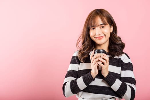 Portrait Asian Thai beautiful happy young woman standing smiling holding take away coffee paper cup, studio shot isolated on pink background with copy space, coffee break