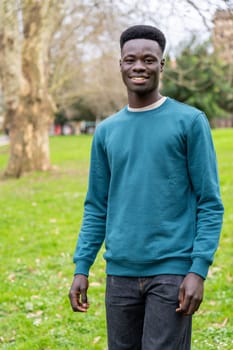 A young man wearing a blue sweater stands in a grassy field. He is smiling and he is enjoying the outdoors