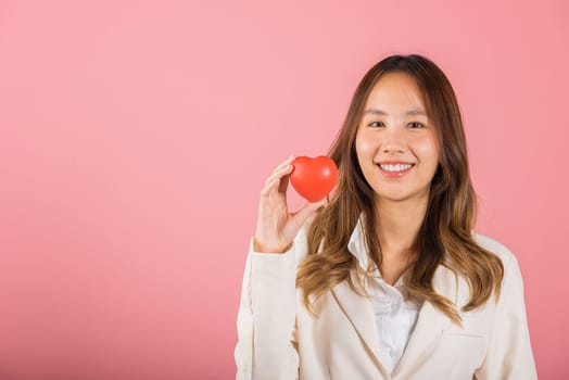 Smiling woman confidence showing holding red heart with her hand palm isolated pink background, Asian happy portrait beautiful young female send love and happy valentine in studio shot, copy space