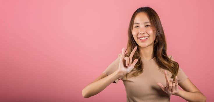 Portrait of Asian young woman showing I LOVE YOU gesture in sign language in studio shot isolated on pink background, Hand sign language, Valentine Day