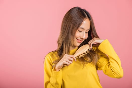 Portrait of Asian beautiful young woman smile combing her hair, happy female long healthy hair with hairbrush brushing hair, studio shot isolated on pink background