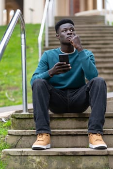 A young man sits on a set of stairs with his cell phone in his hand. He is deep in thought, possibly contemplating something important