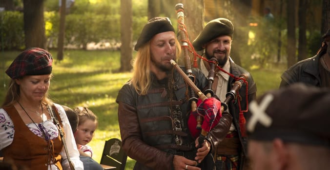 Closeup picture of young man playing pipes in national uniform on green summer outdoors. High quality photo