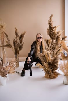 A woman photographer, a blonde with a camera, seriously with sunglasses in the production studio. Wearing a black clothes on a brown background