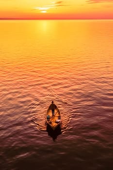 A man is in a canoe on a lake at sunset. The sky is orange and the water is calm