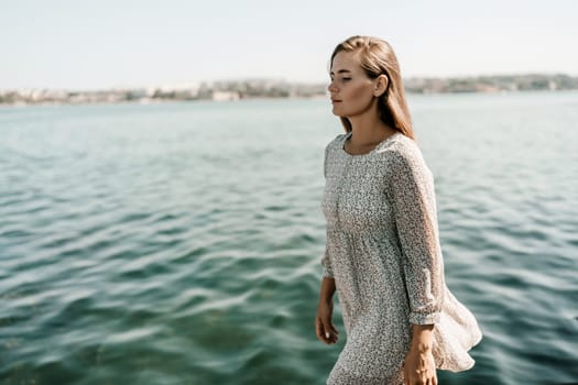 A woman is walking on the beach wearing a dress. The water is calm and the sky is clear