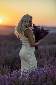 Blonde woman poses in lavender field at sunset. Happy woman in white dress holds lavender bouquet. Aromatherapy concept, lavender oil, photo session in lavender.