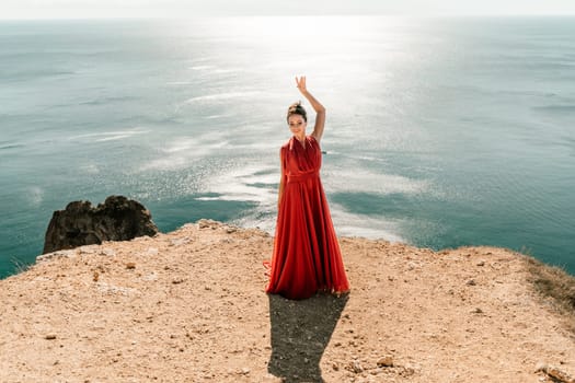 Woman red dress sea. posing on a rocky outcrop high above the sea. Girl on the nature on blue sky background. Fashion photo