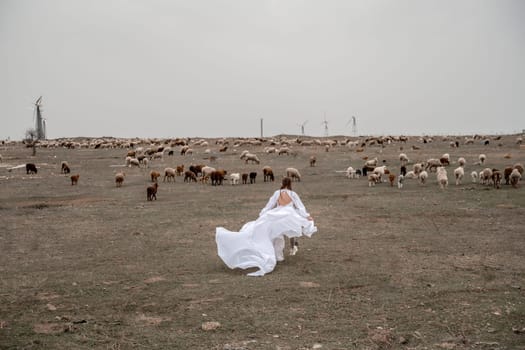 A woman in a white dress is walking through a field of cows. The cows are scattered throughout the field, with some closer to the woman and others further away. The scene has a peaceful