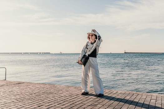 Stylish seashore woman. Fashionable woman in a white hat, white trousers and a light sweater with a black pattern on the background of the sea