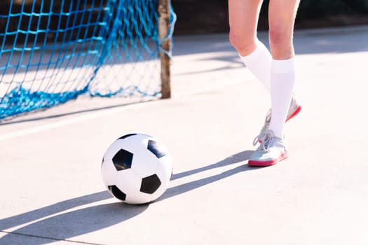 close up of the feet of a soccer player walking towards a soccer ball next to the goal of an urban field, concept of sport and active lifestyle