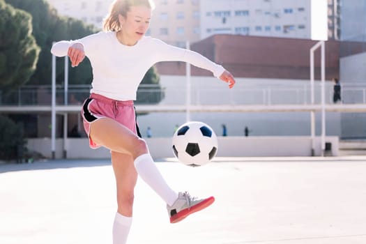 female soccer player kicking the ball with her feet on an urban football court, concept of sport and active lifestyle