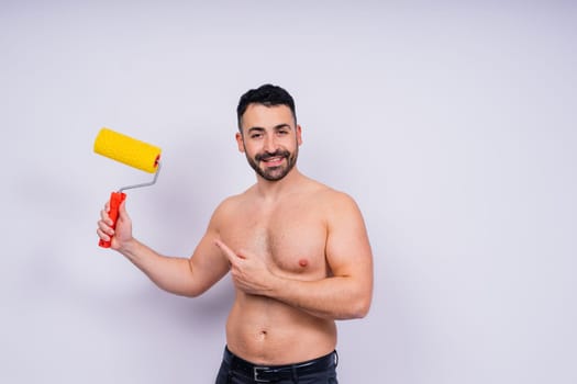 Cheerful young topless man hold paint roller isolated on a grey background studio.