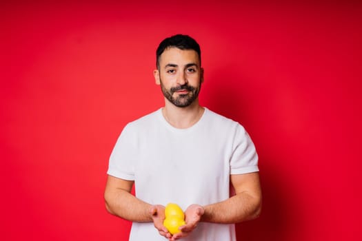 Portrait of young bearded man holding lemons in both hands on an isolated red background