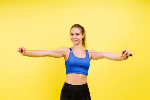 Fit female athlete with jumping with rope during fitness training against yellow background