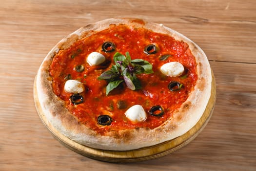 Neapolitan pizza with tomatoes, mozzarella, basil and olives on marble table