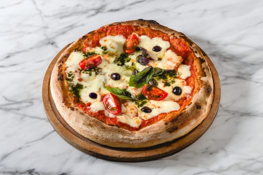 Neapolitan pizza with tomatoes, mozzarella, basil and olives on marble table