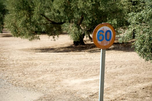 A vintage 60 speed limit sign stands prominently in a deserted rural setting with dusty roads and green foliage, evoking a sense of nostalgia and travel.