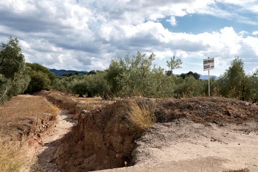 Scenic rural area showing soil erosion with a private hunting sign. The landscape features olive trees under a cloudy sky.