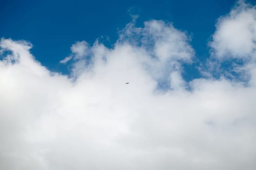 A small airplane flying high in the clear blue sky surrounded by fluffy white clouds. A serene and peaceful scene depicting freedom and travel.