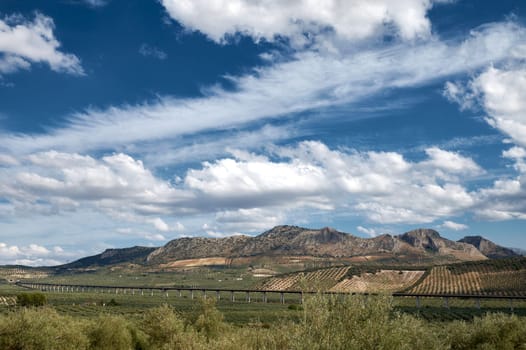 Panoramic view of a mountainous landscape with a railway bridge and clear blue sky dotted with clouds. Ideal for nature, travel, and infrastructure concepts.