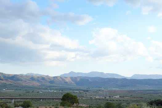 A breathtaking panorama of rolling hills and vast green fields under a partly cloudy blue sky, evoking a sense of tranquility.